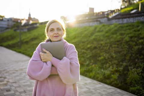 Woman embracing laptop while standing outdoors at sunrise