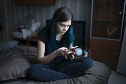 Serious woman using smart phone while sitting on bed