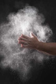 Baker dusting flour off his hands against black background