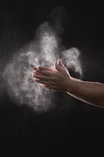 Baker dusting flour off his hands against black background