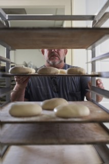 Baker standing with bread dough on tray