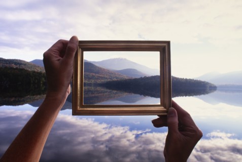Woman's hands holding picture frame up to calm Lake Placid and hills, Lake Placid, New York, USA