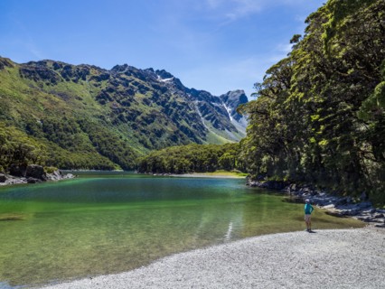 Rear view of woman sitting on lakeshore in Fiordland National Park, Te Anau, Fiordland, New Zealand