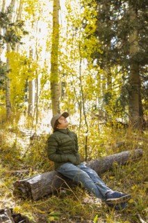 USA, New Mexico, Pensive boy sitting on log in Santa Fe National Forest, Santa Fe, New Mexico, USA