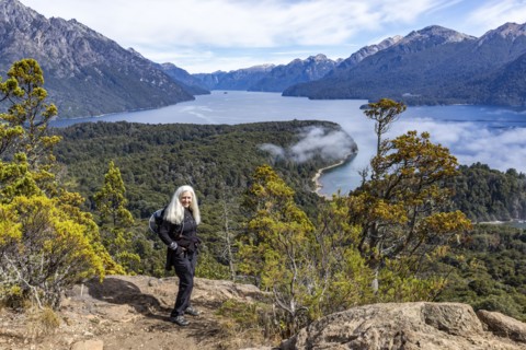 Smiling woman with long white hair standing on top of hill above mountain lakes, Bariloche, ,