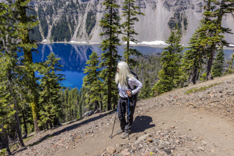 USA, Oregon, Woman with hiking poles on footpath near calm Crater lake