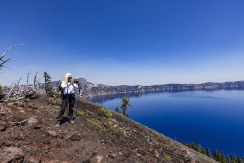 USA, Oregon, Woman with hiking poles taking photos with smart phone by calm Crater lake