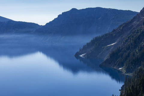 USA, Oregon, Hills reflected in calm, blue Crater lake