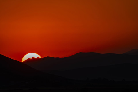 Sun setting behind hills against orange sky