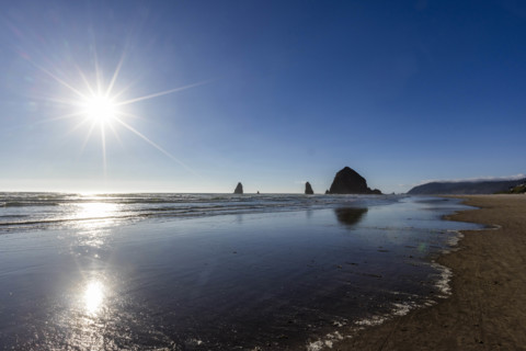 USA, Oregon, Sun setting over ocean and empty Cannon Beach