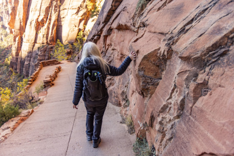 USA, Utah, Zion National Park, Rear view of female hiker touching sandstone cliff on trail to