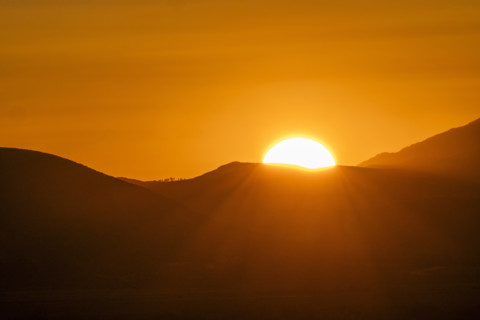 Sun setting above hills against orange sky. Bellevue, Idaho, USA.