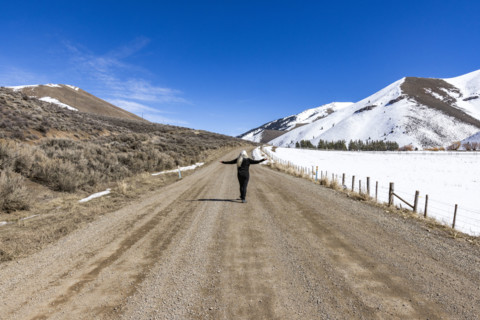 Rear view of woman on empty dirt road in snowy landscape. Bellevue, Idaho, USA.