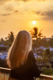 Rear view of blonde woman viewing sunset from deck. Kona, Hawaii, USA.