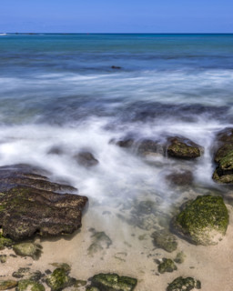 Motion blurred ocean waves washing rocks on beach. Kona, Hawaii, USA.
