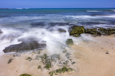 Motion blurred ocean waves washing rocks on beach. Kona, Hawaii, USA.