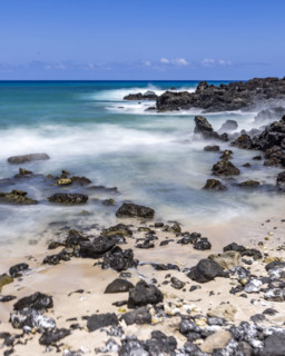 Motion blurred ocean waves washing rocks on beach. Kona, Hawaii, USA.