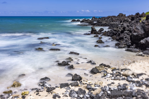 Motion blurred ocean waves washing rocks on beach. Kona, Hawaii, USA.