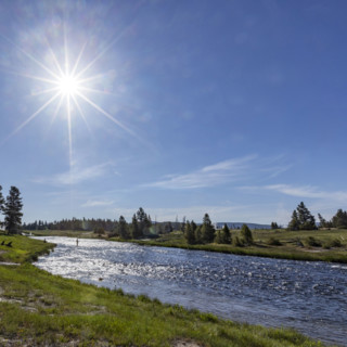 Sun on blue sky over Firehole River. , Wyoming, USA.