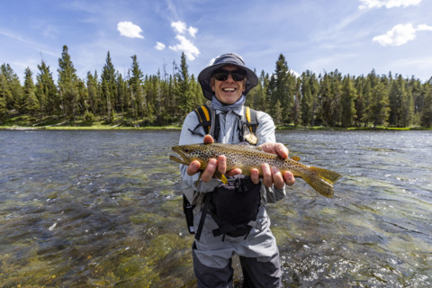 Portrait of smiling fly fisherman holding trout before releasing. , Wyoming, USA.