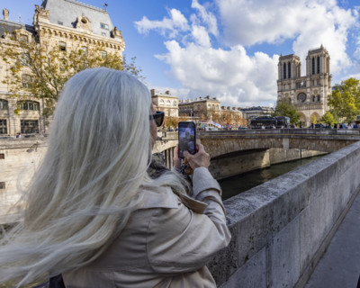 Rear view of blonde woman photographing Notre Dame on smart phone. Paris, Ile de France, France.