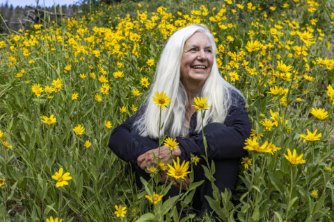 Portrait of senior blonde woman in field of Arrowleaf Balsamroot wildflowers. Sun Valley, Idaho,