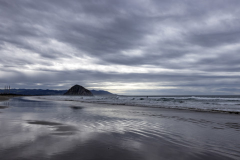 Storm clouds above beach with Morro Rock in distance, Morro Bay, California, USA.