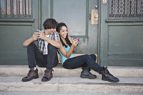 Couple using cell phones on front stoop, Los Angeles, California, USA.