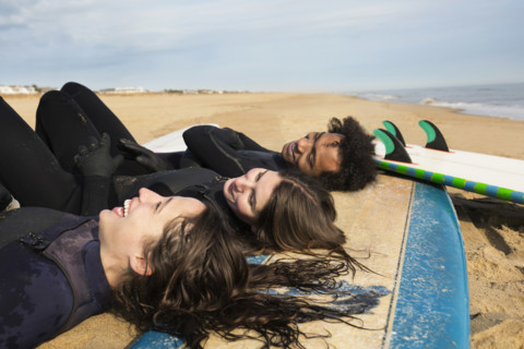 Smiling surfers laying on boards on beach, Virginia Beach, Virginia, USA.