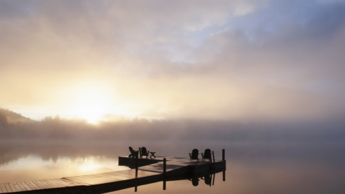 Silhouettes of adirondack chairs on pier on Lake Placid at sunrise