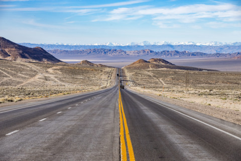 Traffic on desert highway with snowcapped mountains in distance
