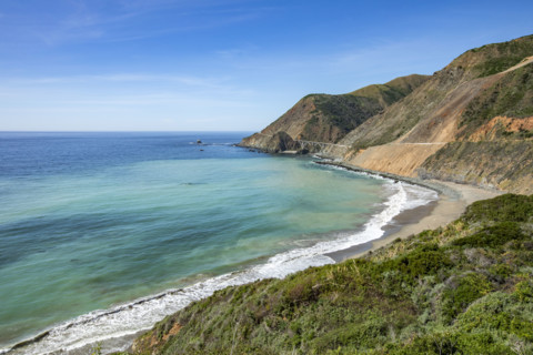 Ocean waves washing Big Sur Coast with Bixby Bridge in distance
