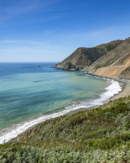 Ocean waves washing Big Sur Coast with Bixby Bridge in distance