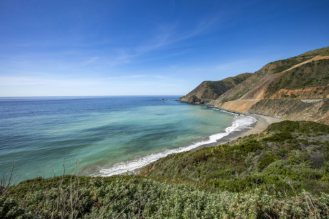 Ocean waves washing Big Sur Coast with Bixby Bridge in distance