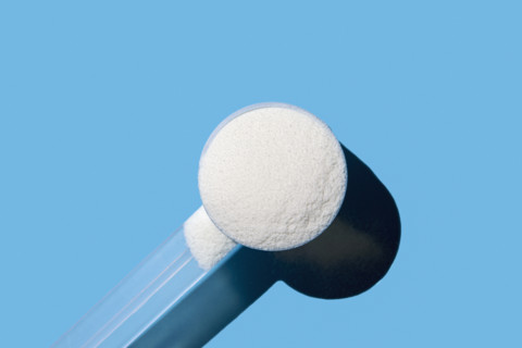 Scoop of collagen powder on blue background