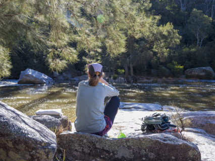 Rear view of woman sitting on rock on riverbank