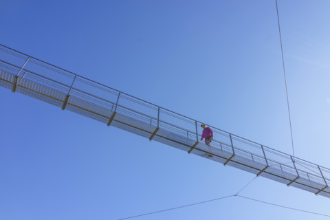 Hiker crossing suspension footbridge against clear sky