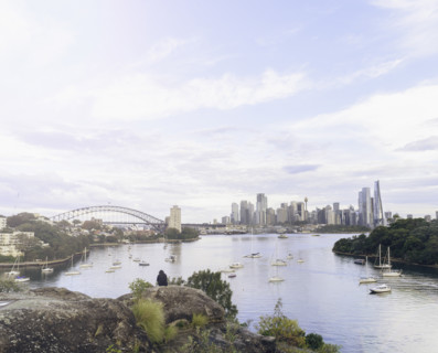 Rear view of person sitting on rock and looking at Sydney skyline