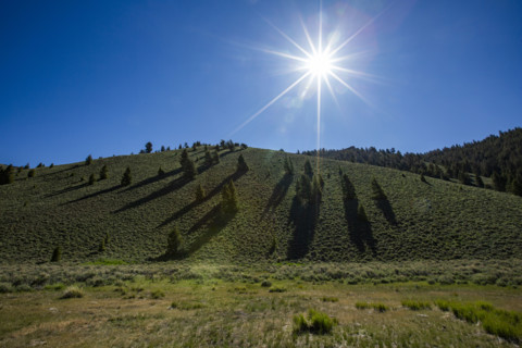 Sun on blue sky above green hill