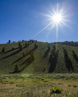 Sun on blue sky above green hill