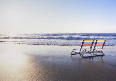 Pair of colorful beach chairs facing ocean at sunrise