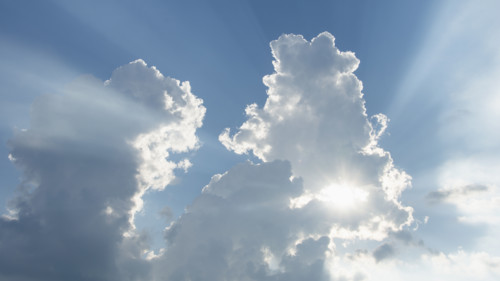 Sun shining through white puffy clouds