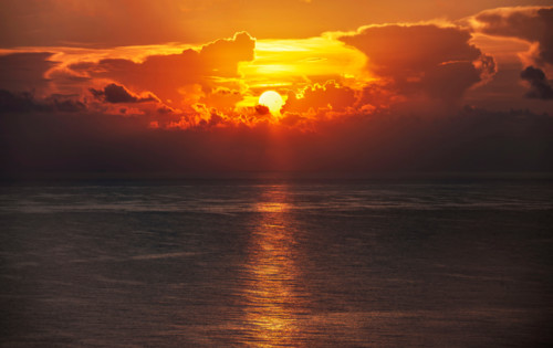 Sun rising through clouds over calm ocean. Boca Raton, Florida, United States