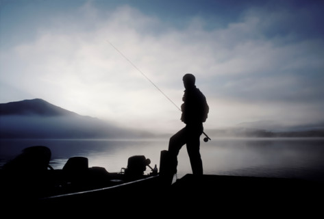 Silhouette of fisherman by calm lake Placid at dawn. Lake Placid, New York, United States