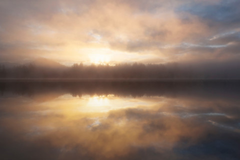 Dramatic sunrise sky reflected in calm lake. Lake Placid, New York State, United States