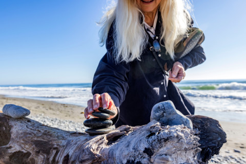 Woman stacking rock cairn on beach. Gold Beach, Oregon, United States