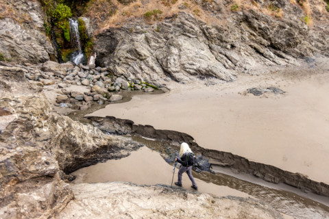 Woman approaching waterfall on Oregon Coast beach. Gold Beach, Oregon, United States