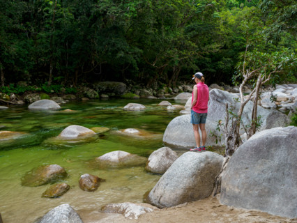 Rear view of tourist standing on boulder in Mossman River. Mossman, Queensland, Australia