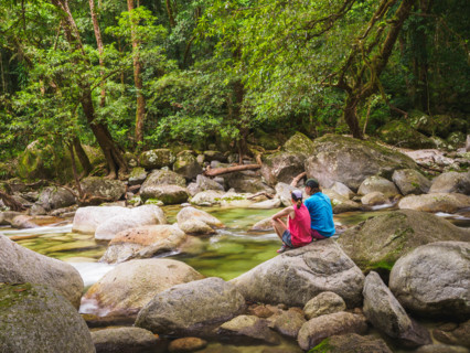Rear view of couple sitting on boulder in Mossman River. Mossman, Queensland, Australia
