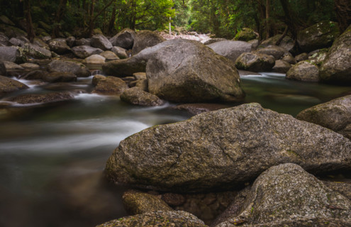 Long exposure of water flowing around rocks in fast moving river. Mossman, Queensland, Australia